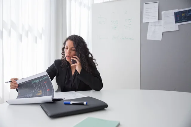 Focused businesswoman reviewing data charts during a phone call in a modern office setting. AI in B2B demand generation: workflow and oversight