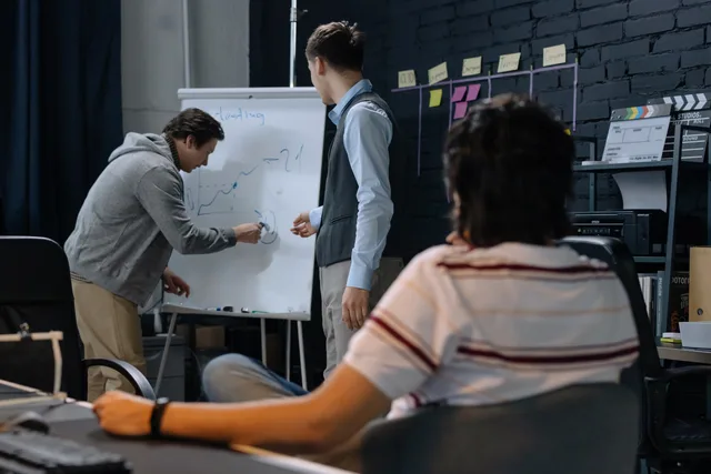 Team members brainstorming at work discussing a business strategy on a whiteboard. Run B2B demand generation audience research: a practical guide