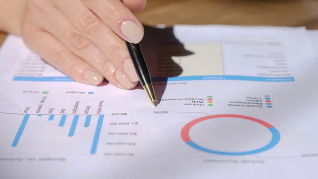 Close-up of a hand with a pen pointing at a financial document with graphs and charts. Why B2B demand generation hidden costs erode your budget