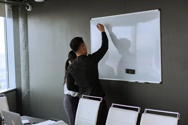 Two professionals brainstorming on a whiteboard during a work meeting. When to write your B2B demand generation software rubric
